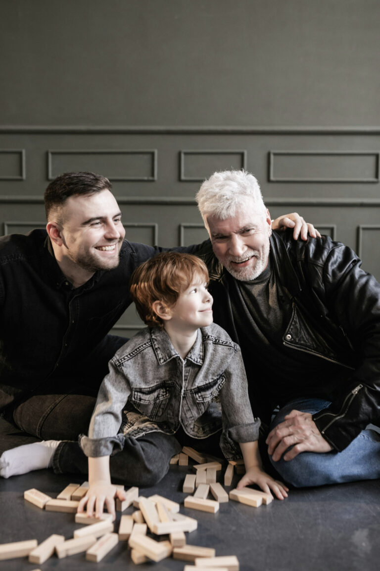 A father, son, and grandfather sit on a floor and play with blocks. 3 generations in one picture. This article covers what families should know before helping parents downsize.