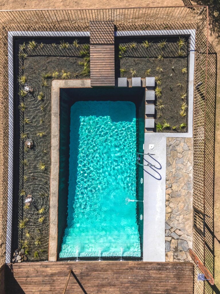 A bird's eye view of an in-ground pool surrounded by plants and cobblestone. This article covers what to expect when building a custom pool.