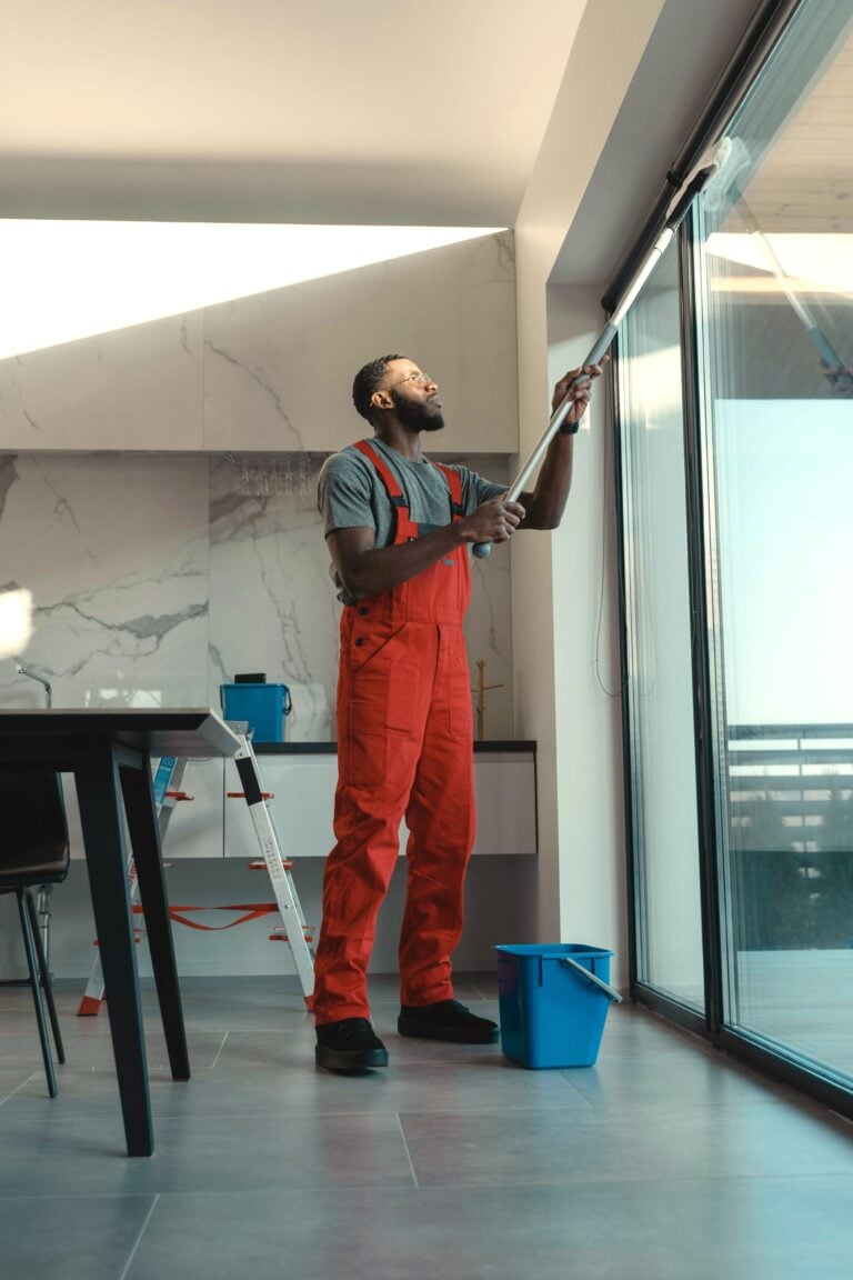 A man cleans ceiling to floor windows inside a modern home. This article covers how to choose the right window cleaning service in Encinitas.