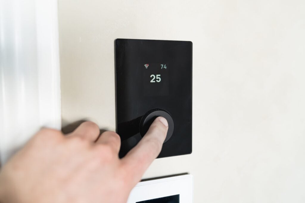 A person presses a button on a smart thermostat. This article covers how to enhance home safety and efficiency with electrical upgrades.