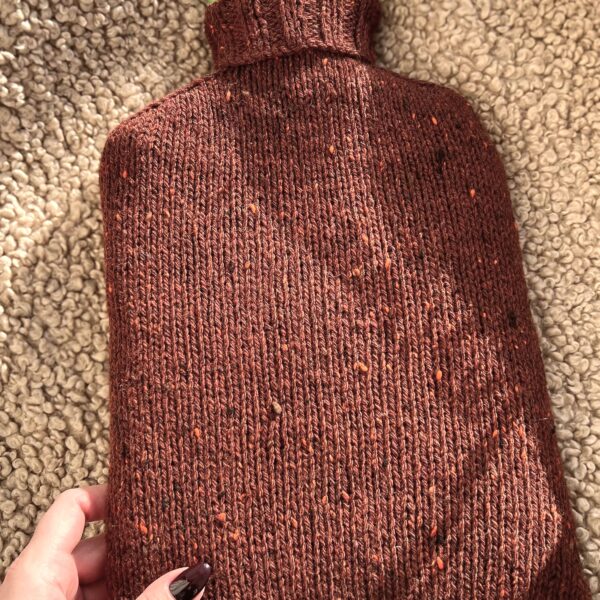 A hot water bottle wrapped in wool sits on a cozy sheepskin blanket. This article helps you learn how long you should use a hot water bottle for effective pain relief.