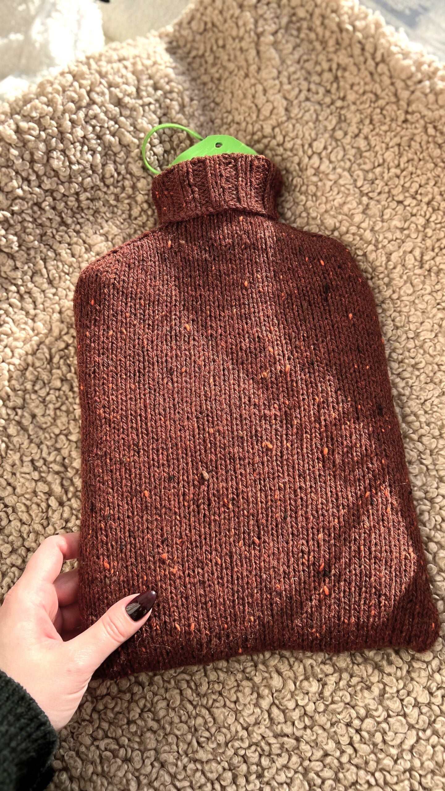 A hot water bottle wrapped in wool sits on a cozy sheepskin blanket. This article helps you learn how long you should use a hot water bottle for effective pain relief.