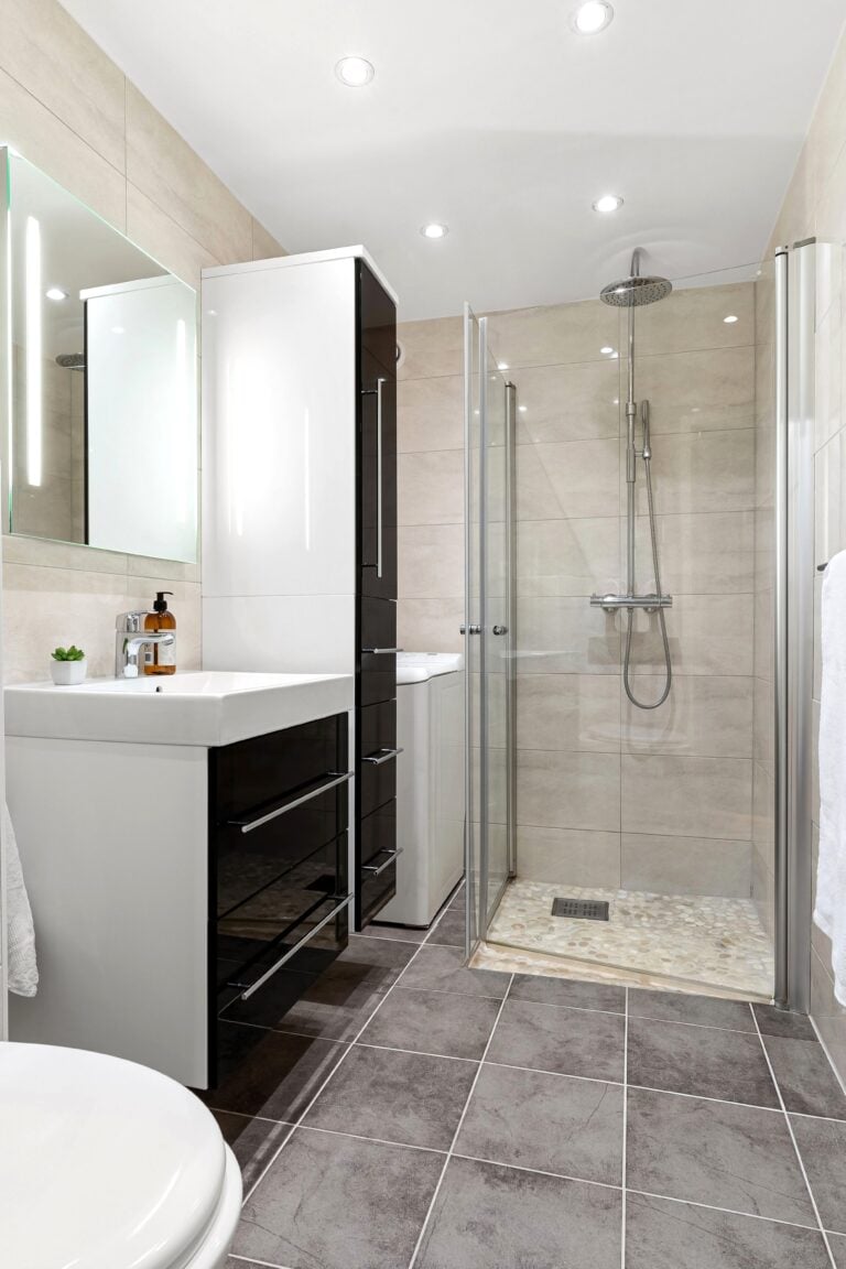 A black and white modern shower with beige tiled walls. This article covers smart shower upgrades that make daily life easier.