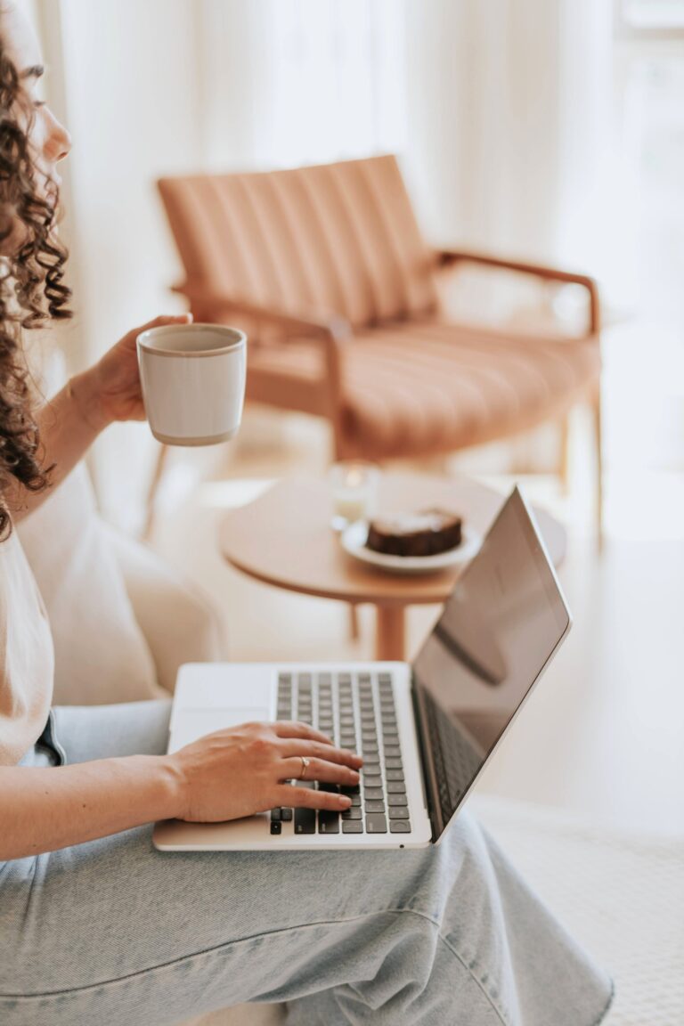 A woman holds a coffee cup and in is working on laptop. This article discusses if you can keep your savings while on disability.
