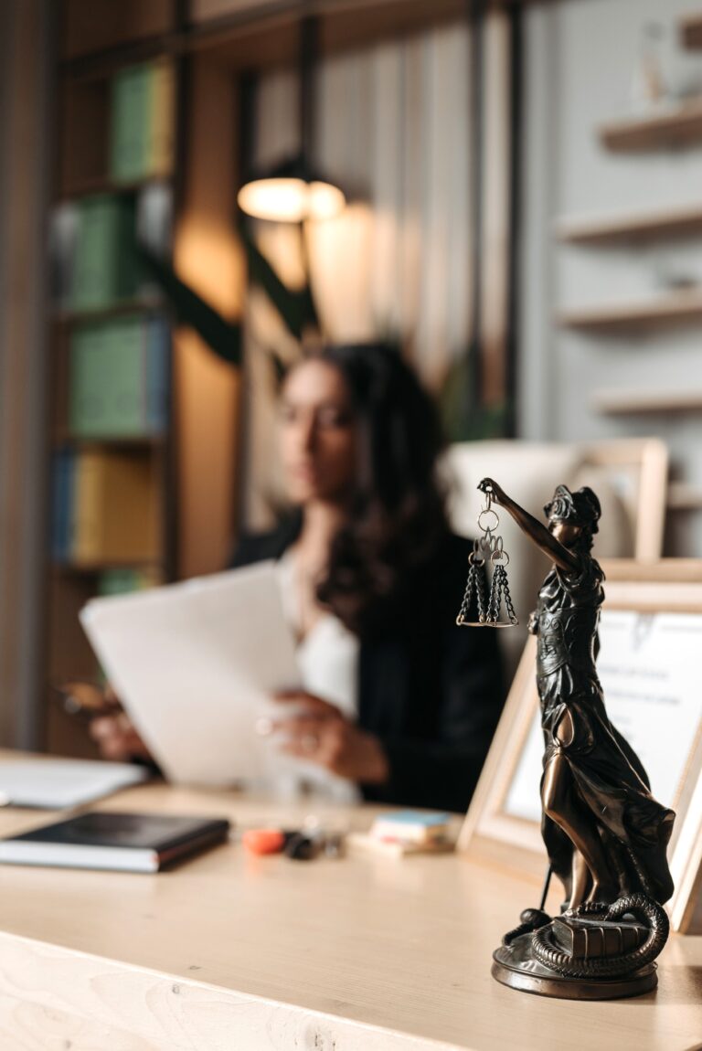 A female lawyer is sitting on a desk in the background and the main focus is Lady Justice statue on the desk. This article helps answer the question, how can a personal injury lawyer help?