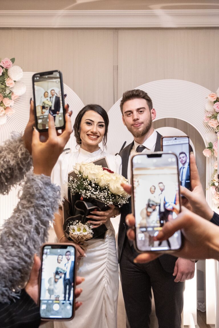 Joyful bride and groom pose with friends capturing memories on smartphones at their wedding celebration. This article shares why couples are switching to online invites and photo sharing.