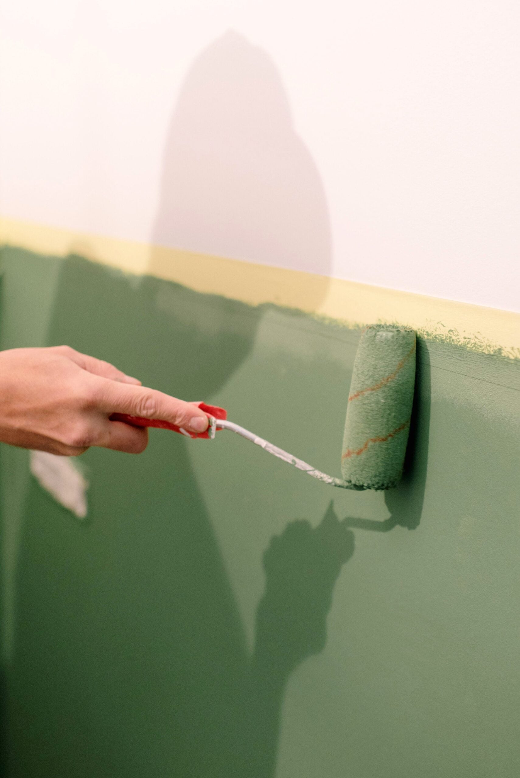 A person using a green paint roller to paint a wall indoors. This article shares how weather affects painting projects.