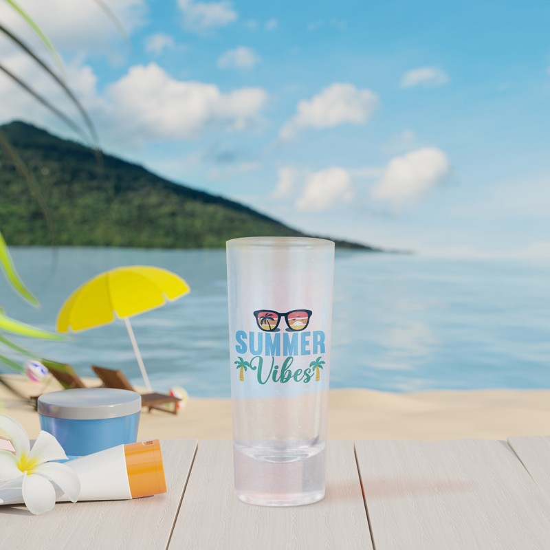 A generic souvenir shot glass in a beach setting.