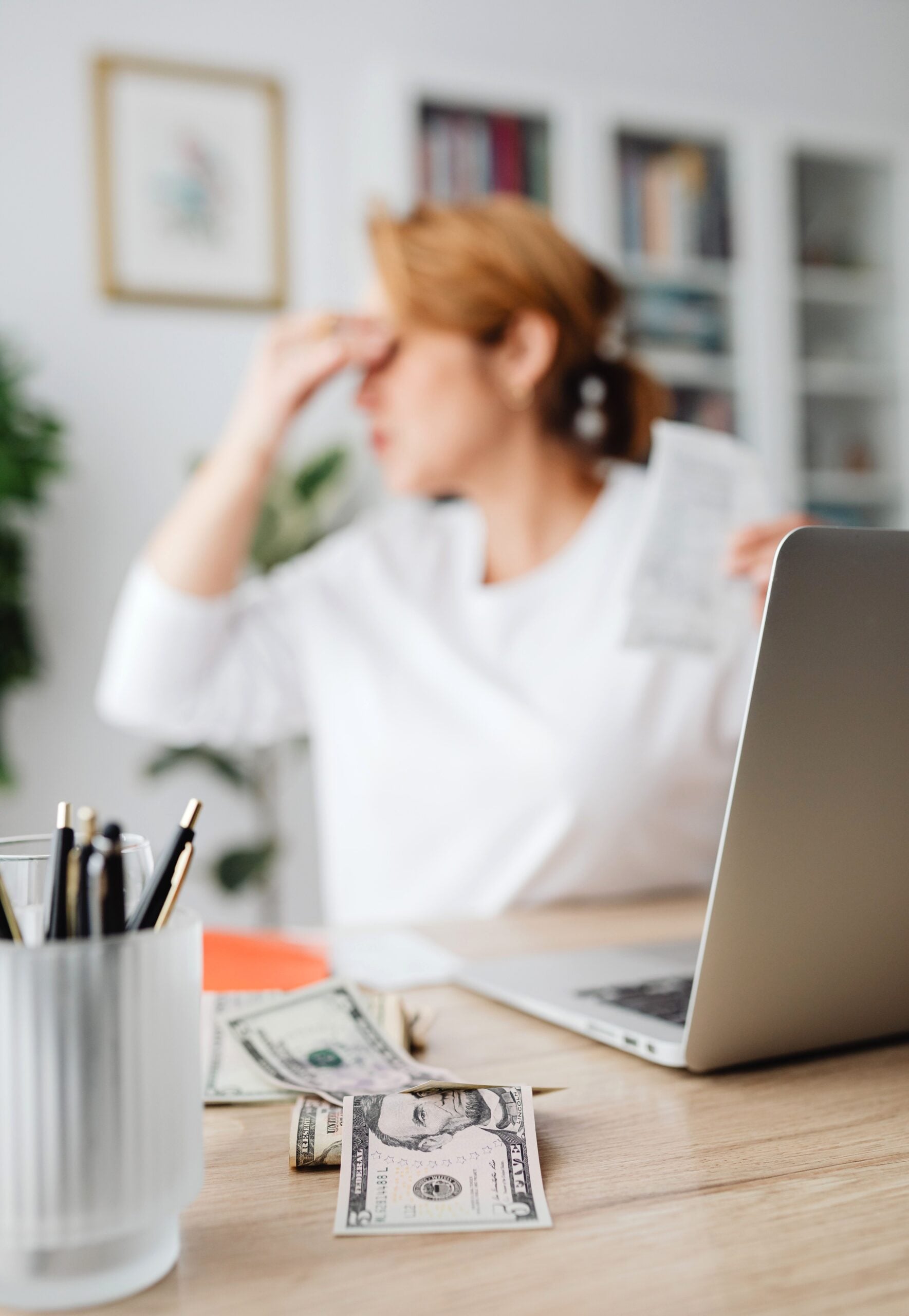 A woman in an office setting feeling stressed over finances, with a laptop and money on the desk. This article answers the question: is a debt relief program for you?