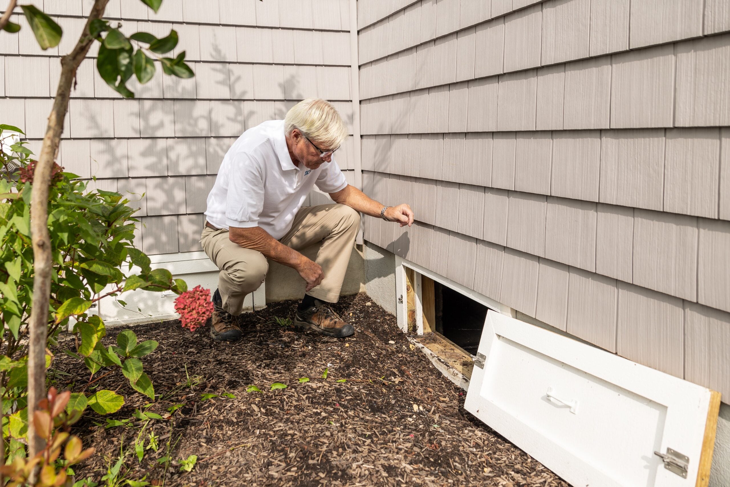 Senior adult inspecting a crawl space entrance during a home inspection on a sunny day. This article shares signs you need a new roof.