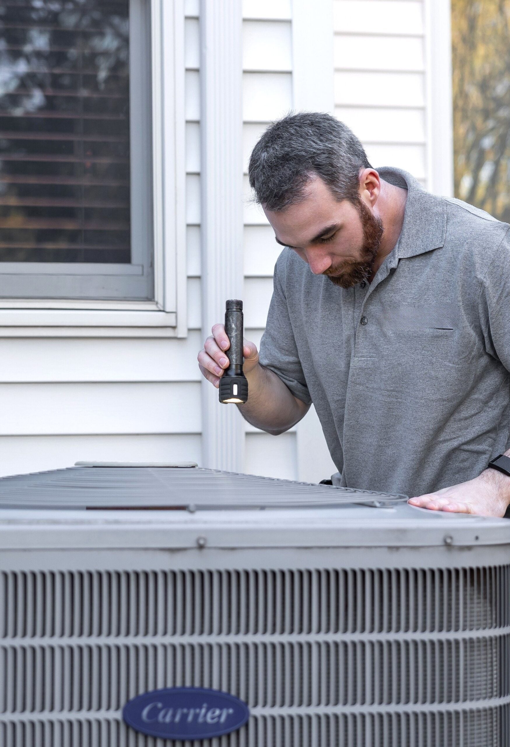 A technician inspects an outdoor HVAC unit for maintenance. This article shares how homeowners end up overpaying for plumbing and HVAC repairs.