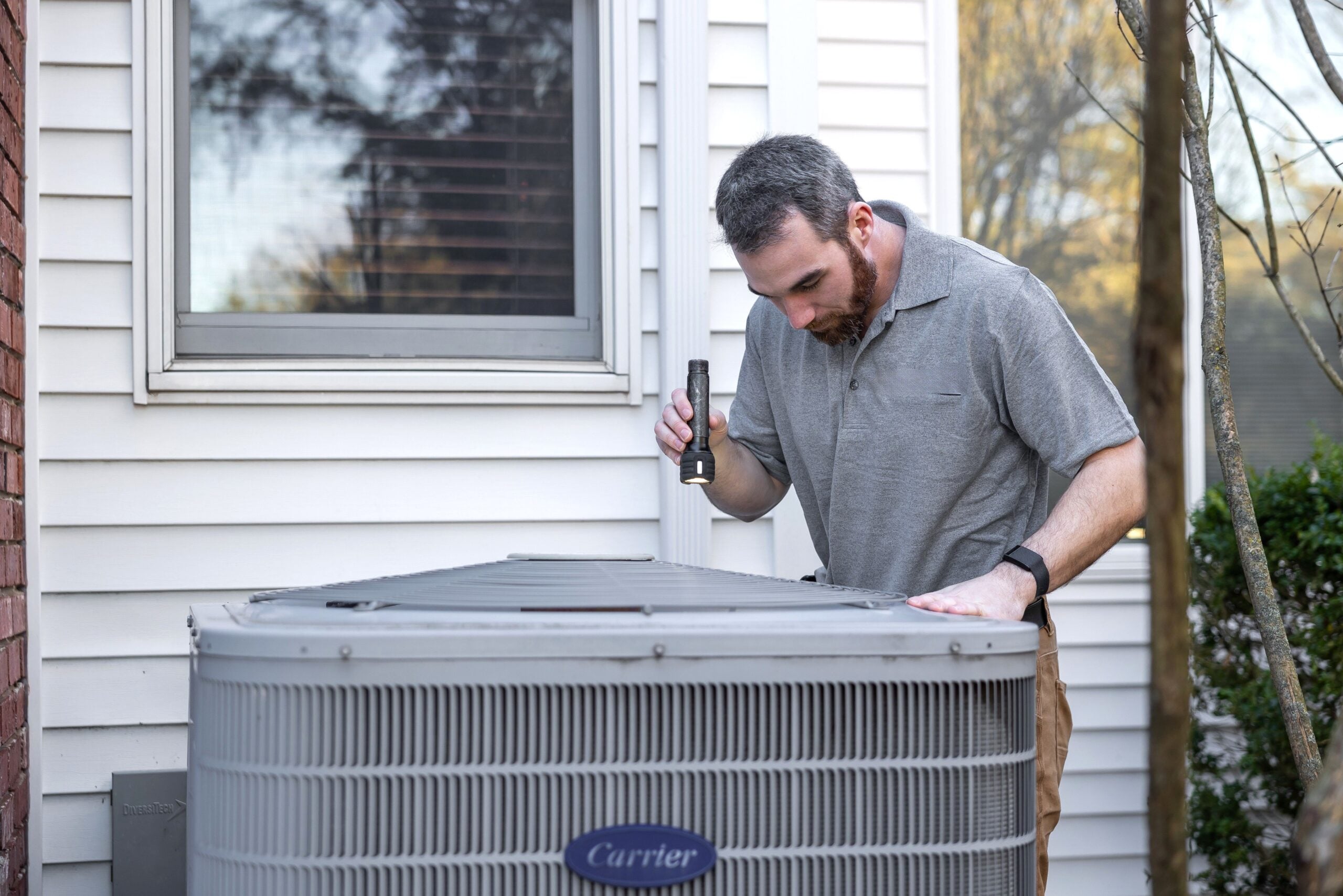 A technician inspects an outdoor HVAC unit for maintenance. This article shares how homeowners end up overpaying for plumbing and HVAC repairs.