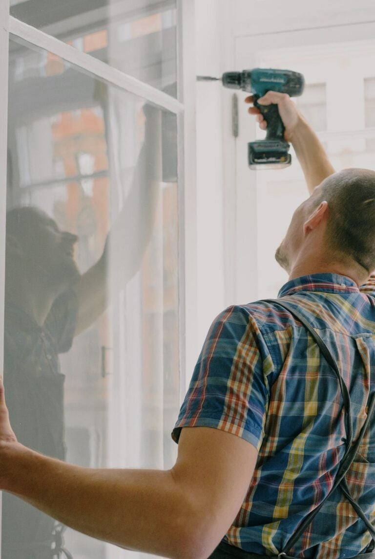 Man installing window indoors with a drill, focusing on home renovation. This article shares when to repair or replace a window.