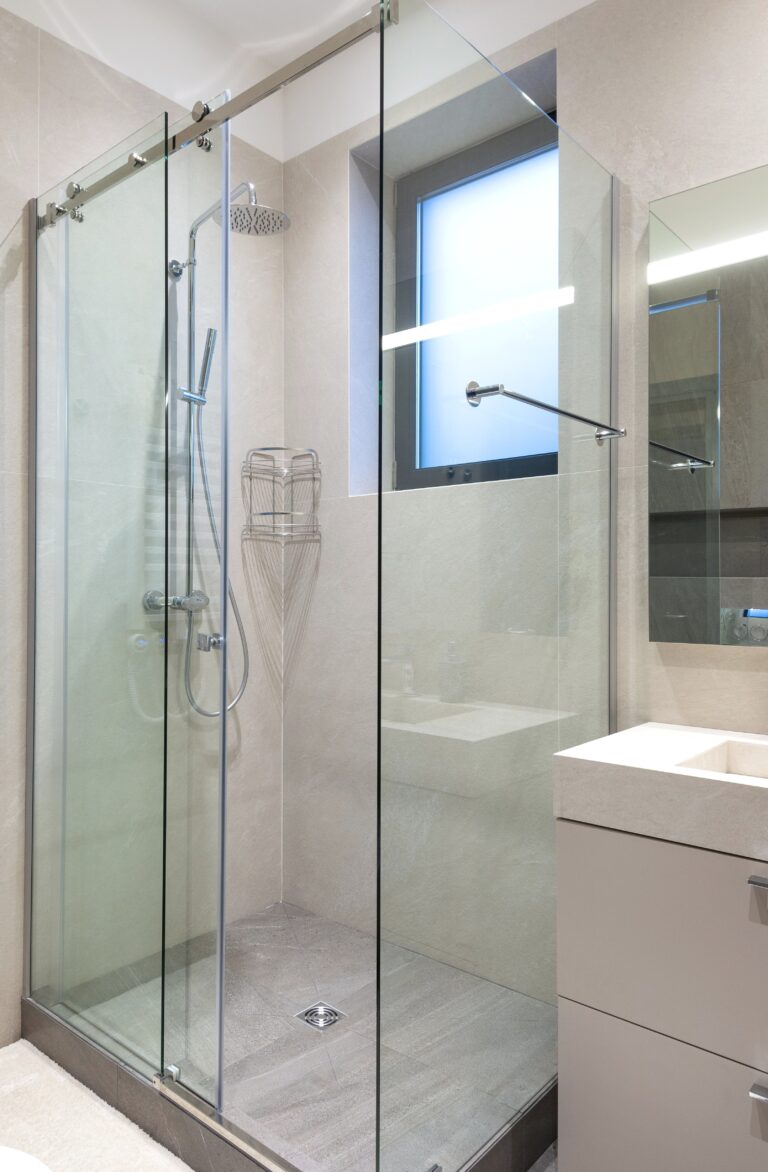 Contemporary bathroom interior featuring glass shower, sink, and mirror in natural tones. This article shares what you need to know before you replace your shower.