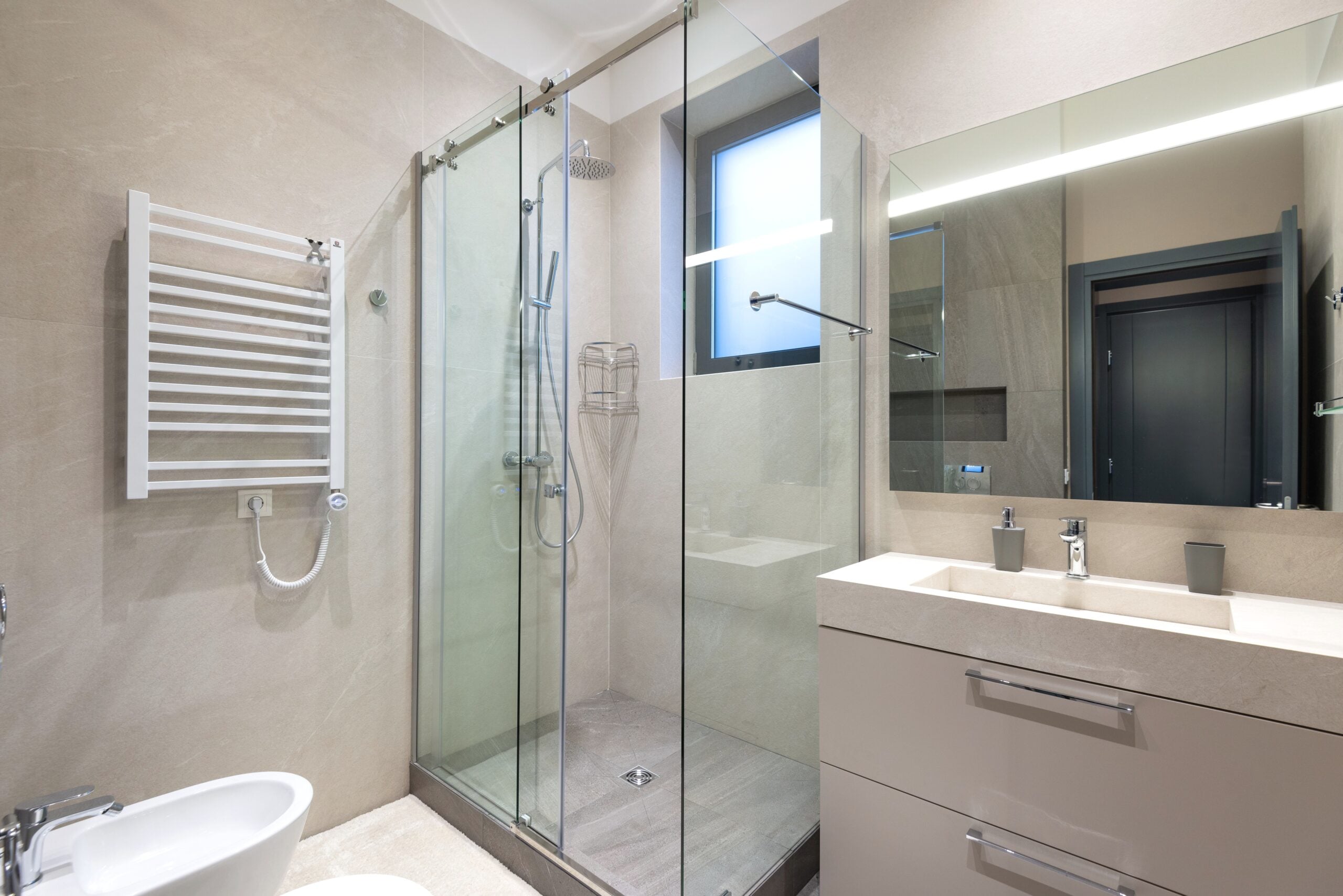 Contemporary bathroom interior featuring glass shower, sink, and mirror in natural tones. This article shares what you need to know before you replace your shower.