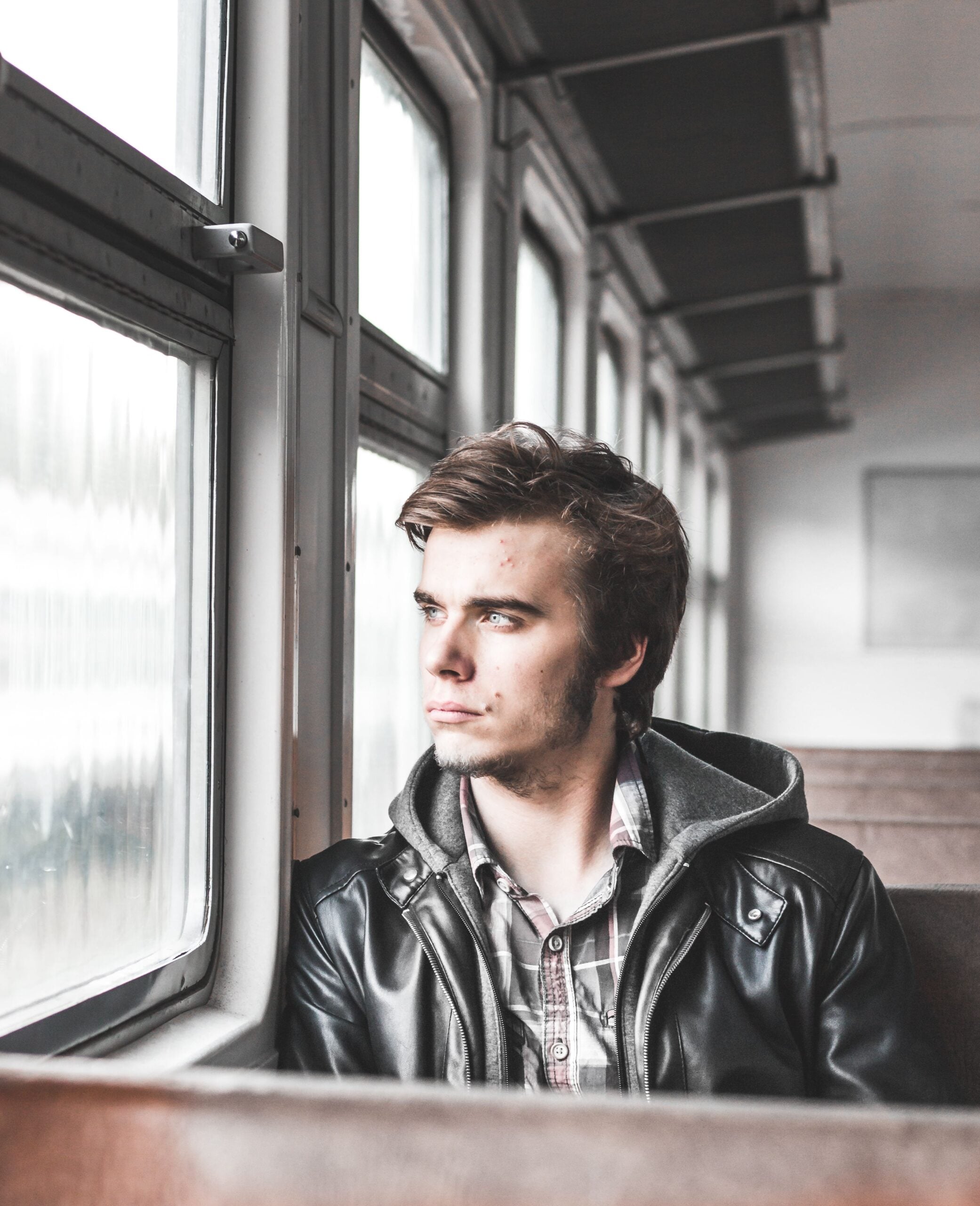 Man in a leather jacket gazing out a train window, deep in thought. This article shares how a DUI charge can quietly disrupt everyday life.