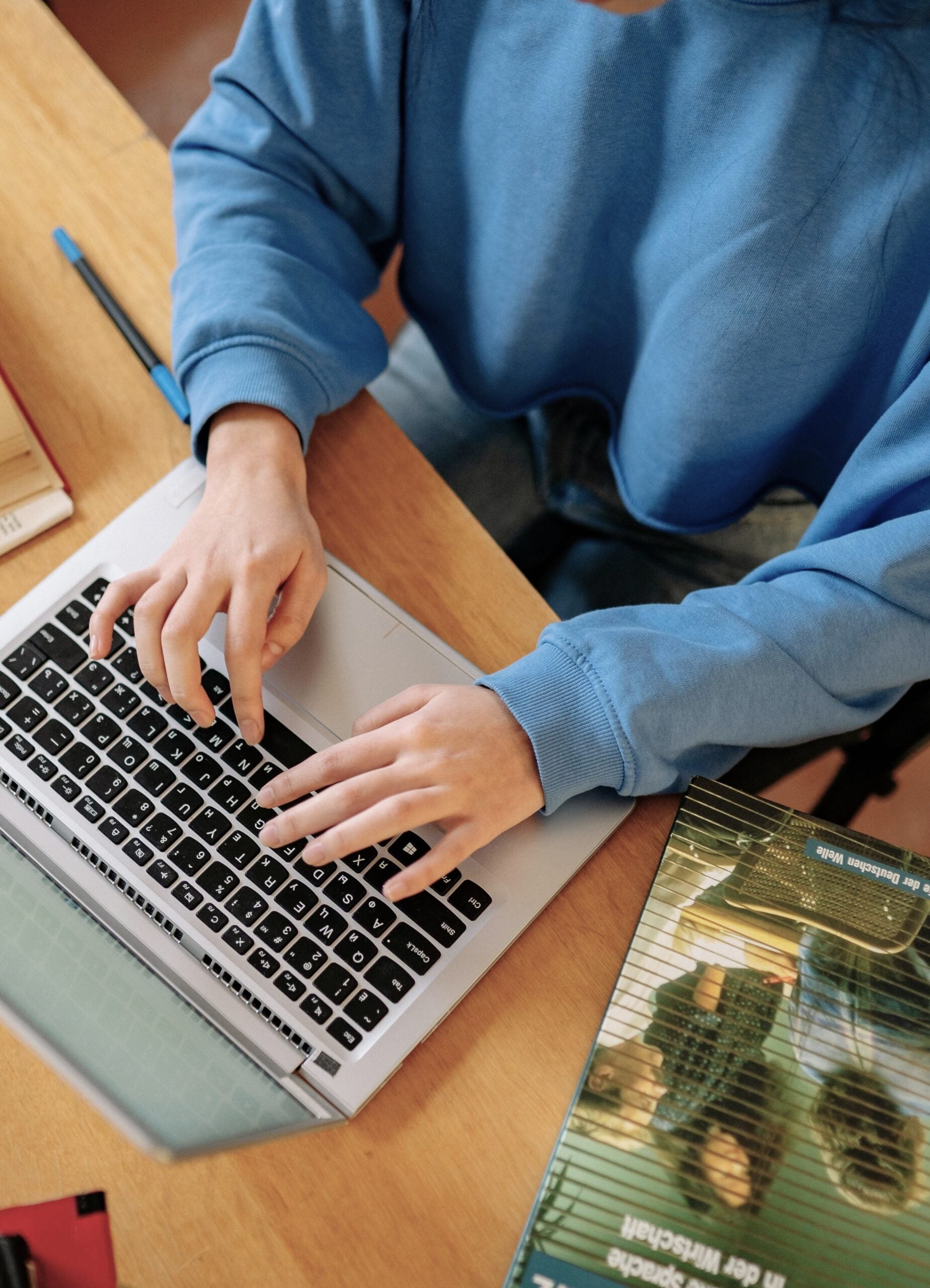 A student typing on a laptop surrounded by open books, focusing on research and school work. This article shares how online prep schools are changing the way you learn.