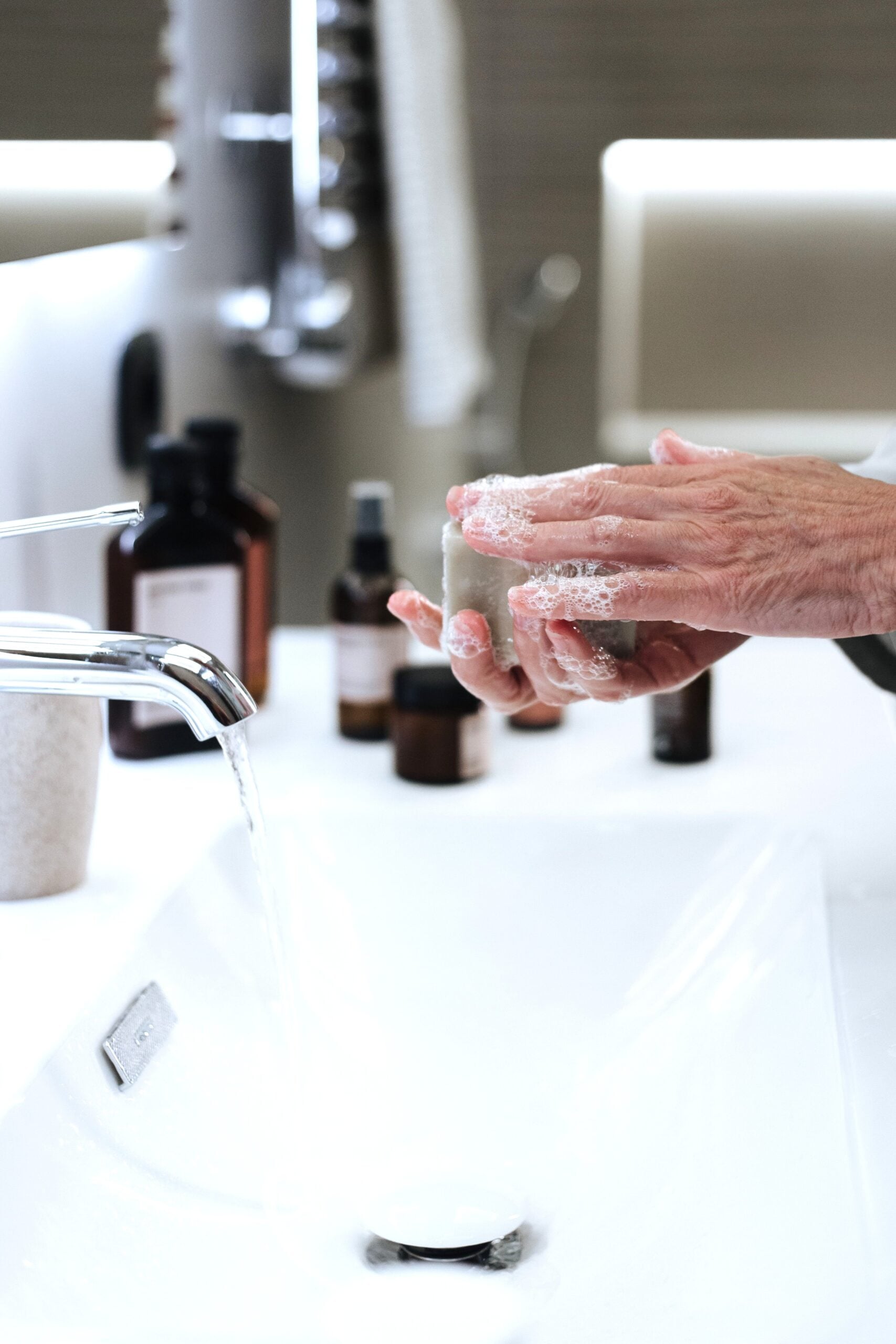 Close-up of hands washing with soap by a running faucet in a stylish bathroom. This article shares how to create an aging in place bathroom design.