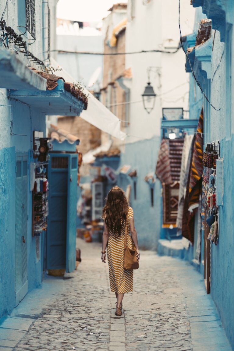 A woman wanders through the vibrant blue alleyways of Chefchaouen, Morocco. This article shares why some of the best travel memories happen at a slower pace.