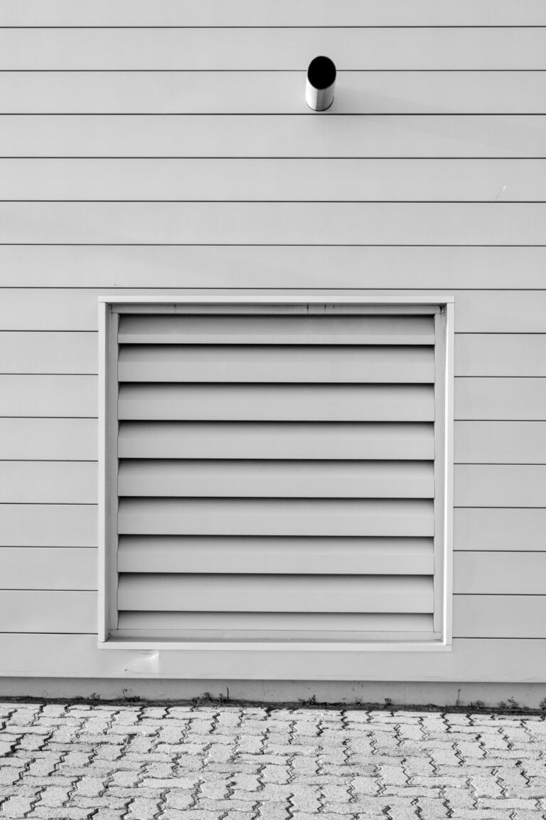 Black and white minimalist photo of an exterior wall with a vent and piping, capturing modern architecture. This article shares the top air duct cleaning companies in Charleston, SC.