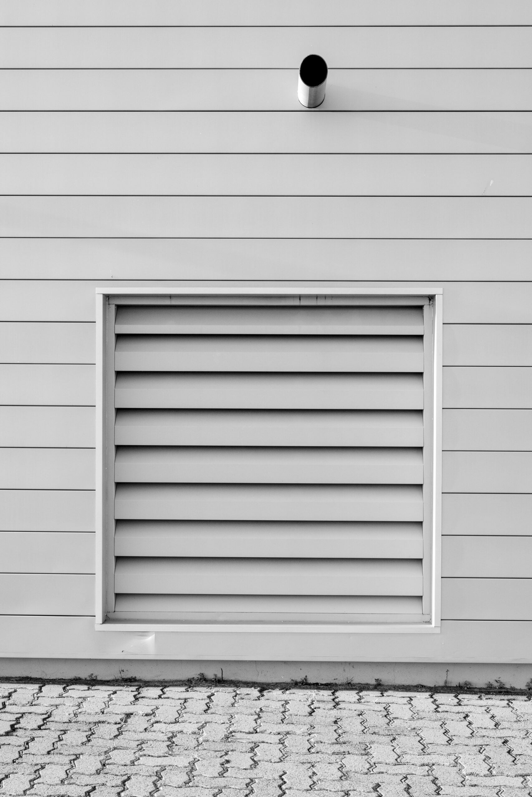 Black and white minimalist photo of an exterior wall with a vent and piping, capturing modern architecture. This article shares the top air duct cleaning companies in Charleston, SC.