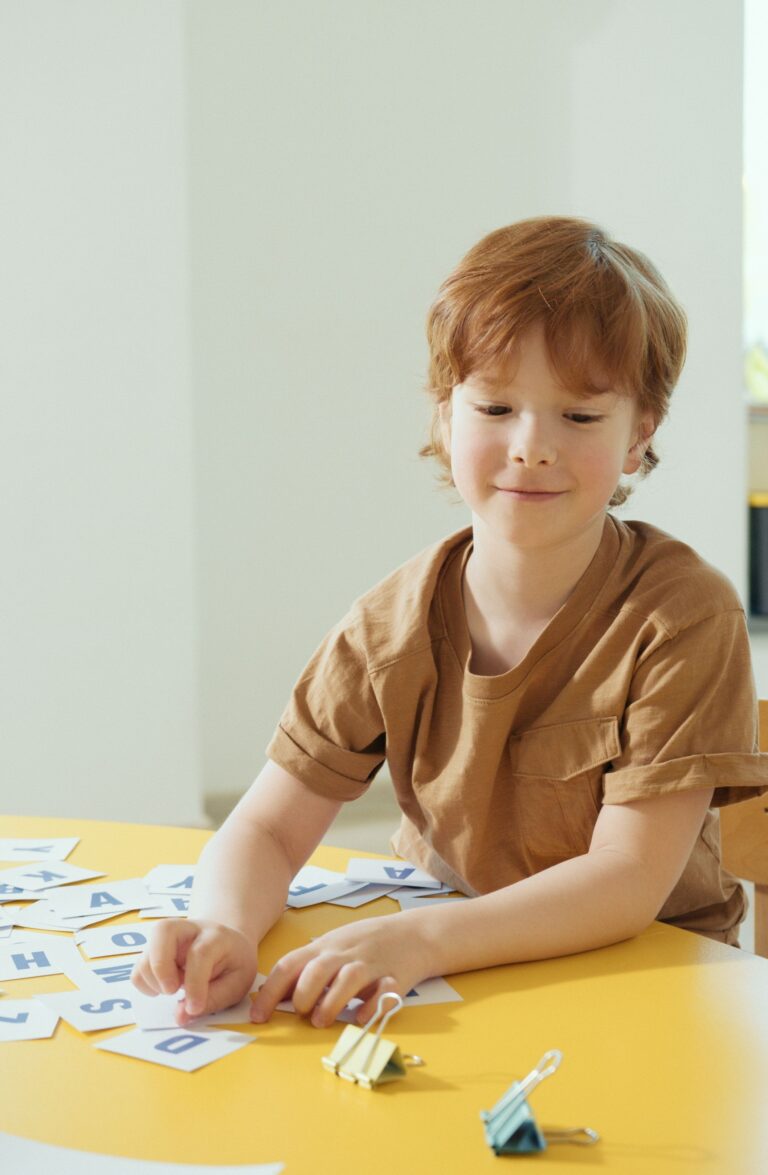 A young boy engaging with letter cards in a bright kindergarten classroom. This article shares how ABA therapy can help you understand your child better.