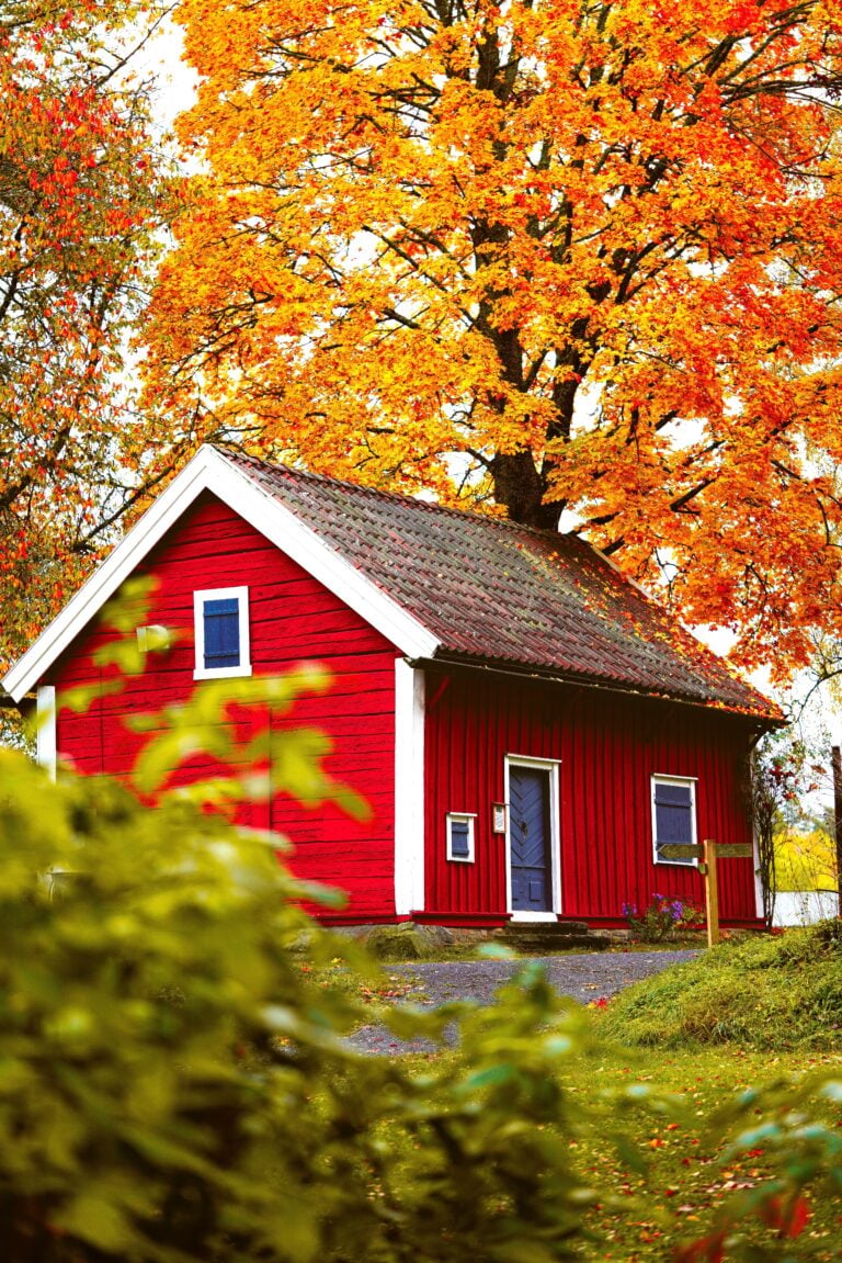 A picturesque red cabin surrounded by vibrant autumn foliage. This article shares a North Okanagan Fall Yard and Home Prep calendar.