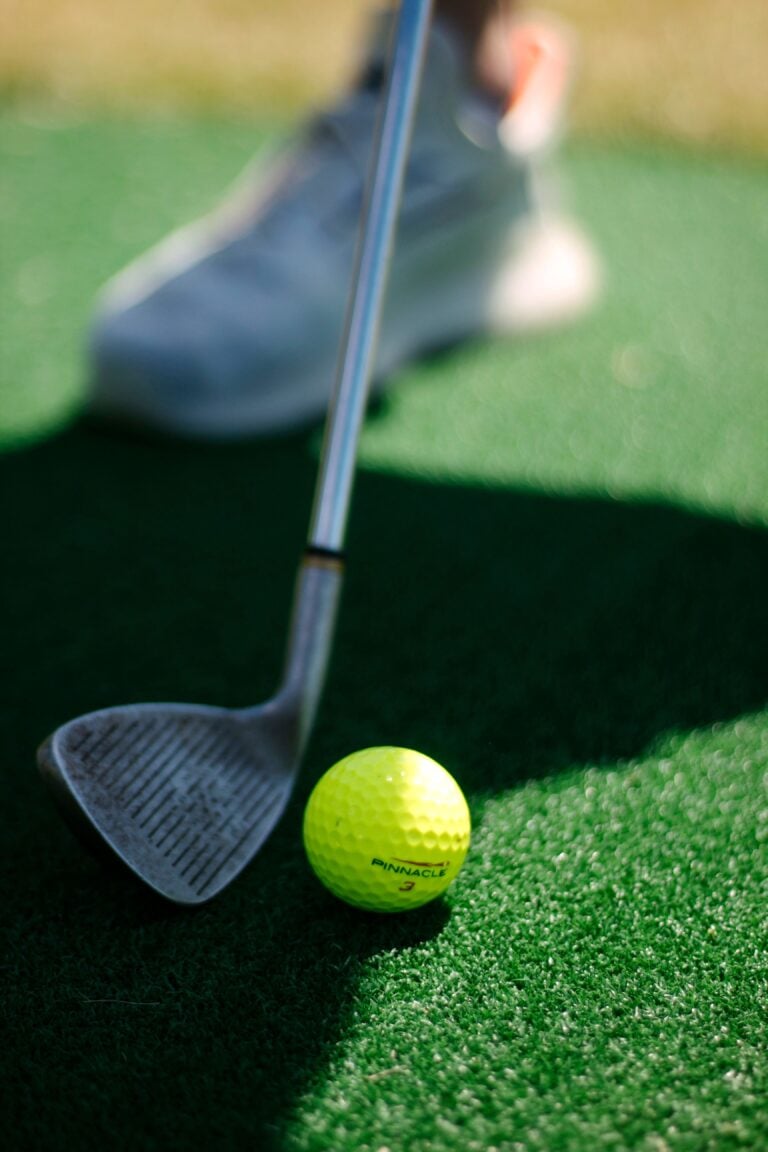 Close-up of a golf club and neon ball on a green turf, perfect for sports enthusiasts. This article covers the top 4 golf simulators that will help you up your golf game.