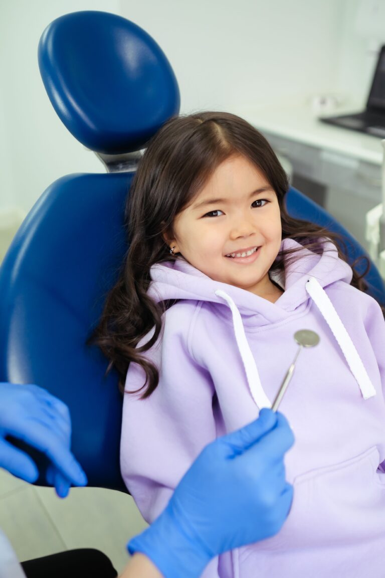 A young girl smiling while sitting in a dental chair, ready for her dental check-up. This article shares reasons families are choosing dental plans for everyday oral care.
