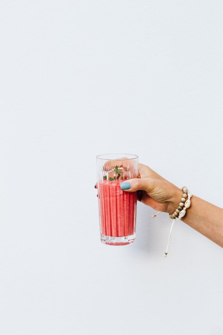 A close-up of a woman's hand holding a healthy pink smoothie in a glass against a minimalistic background. This article covers why functional wellness products are becoming part of modern daily routines.