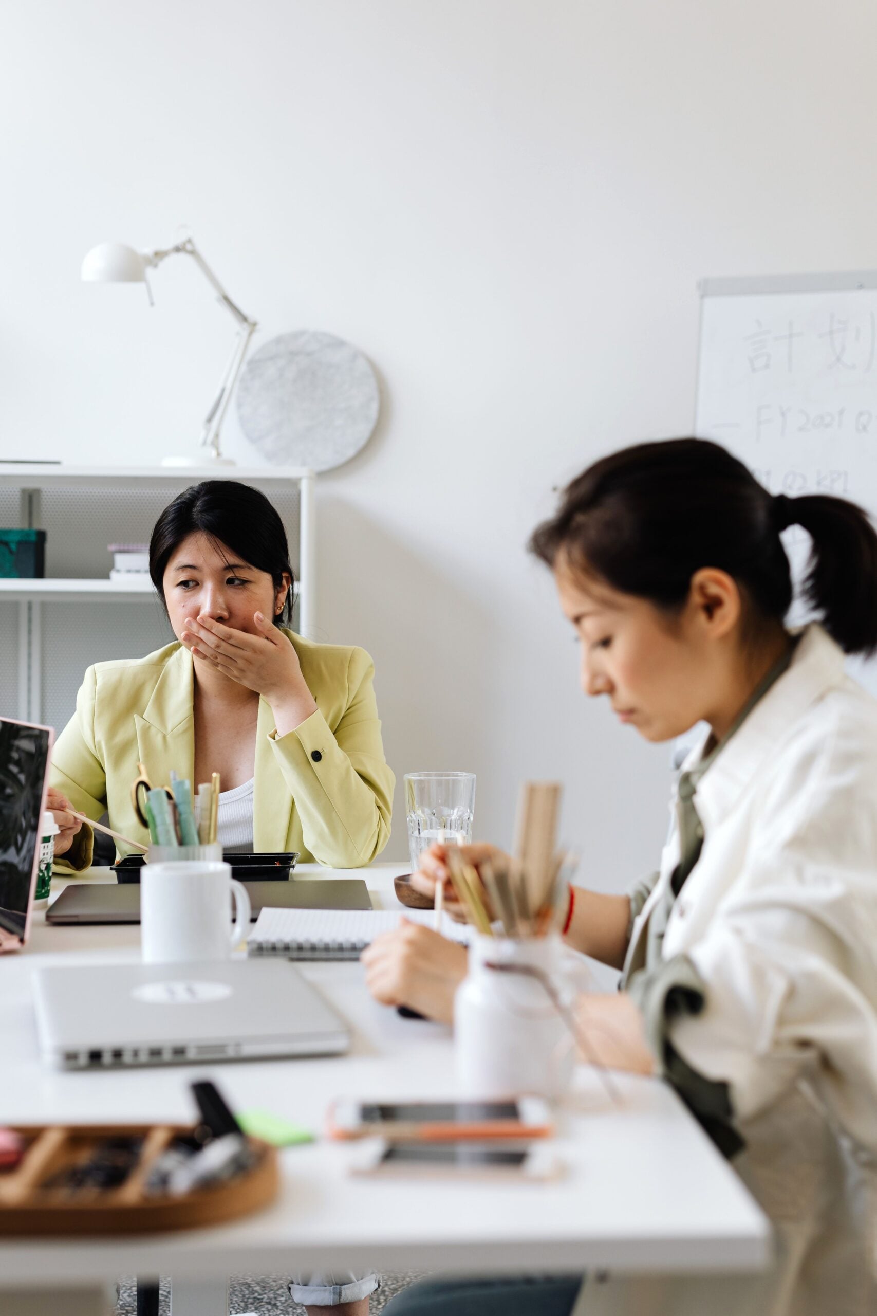 Two women working together in a modern office, one covering her mouth during a discussion. This article covers how to stop sulphur burps on Mounjaro.