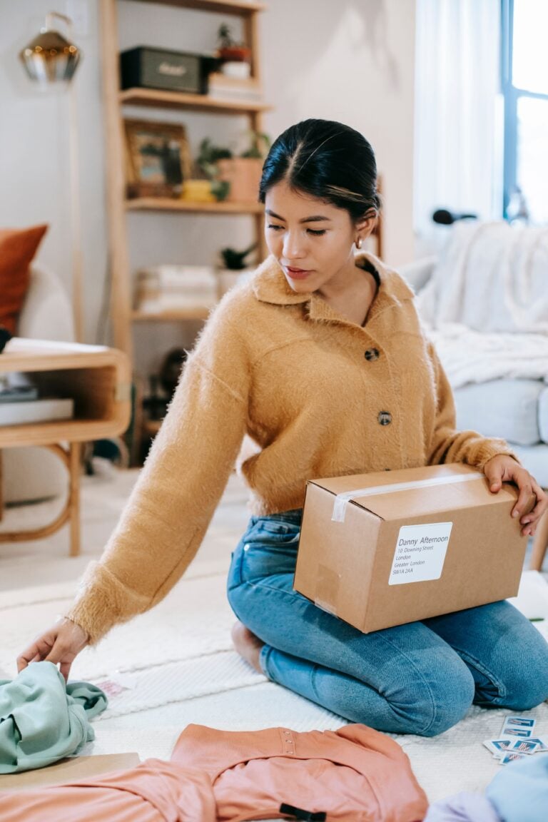 A young woman packs clothing items into a box in a cozy living room setting. This article helps you plan a smarter home cleanout.