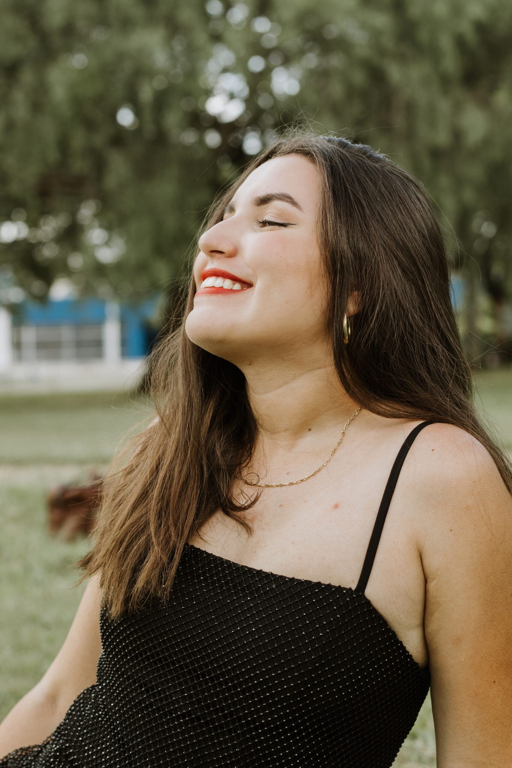 A young woman in a black dress smiling with joy outdoors, embodying happiness and relaxation. This article shares how to create a wardrobe for real life.