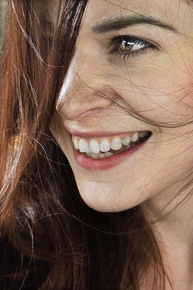 Close-up of a woman smiling with brown hair, capturing joy and natural beauty. This article shares what your mouth can reveal about your health.
