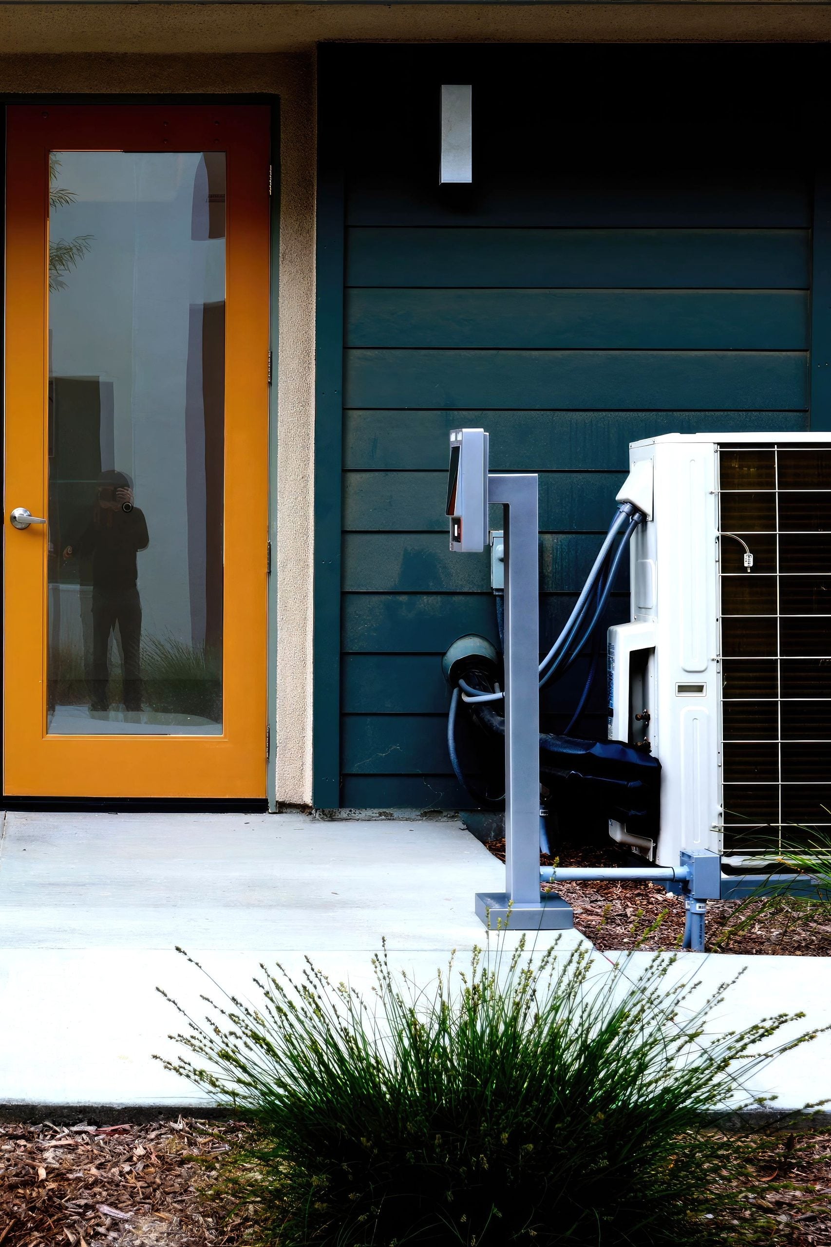 A modern house entrance featuring a yellow glass door and air conditioning unit outside. This guide shares if you should repair or replace your ac.