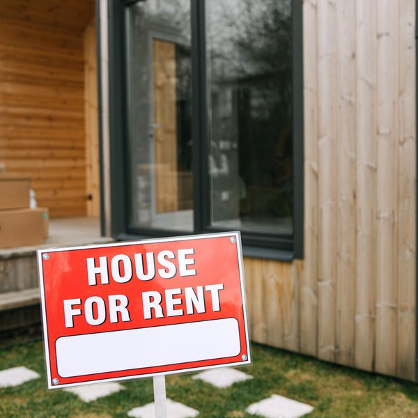 A modern wooden house with a bold 'House for Rent' sign on a grassy lawn, showcasing rental opportunity. This article answers the question, what credit score do you need to rent a house?