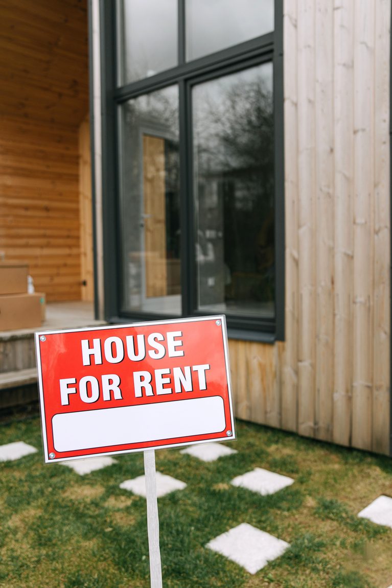 A modern wooden house with a bold 'House for Rent' sign on a grassy lawn, showcasing rental opportunity. This article answers the question, what credit score do you need to rent a house?