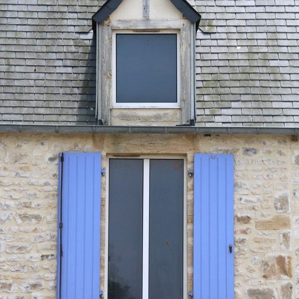 Charming stone wall facade with blue shutters, featuring classic architecture. This article shares when to repair a roof or replace it.