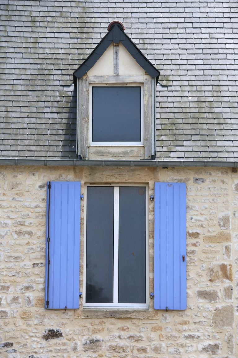 Charming stone wall facade with blue shutters, featuring classic architecture. This article shares when to repair a roof or replace it.