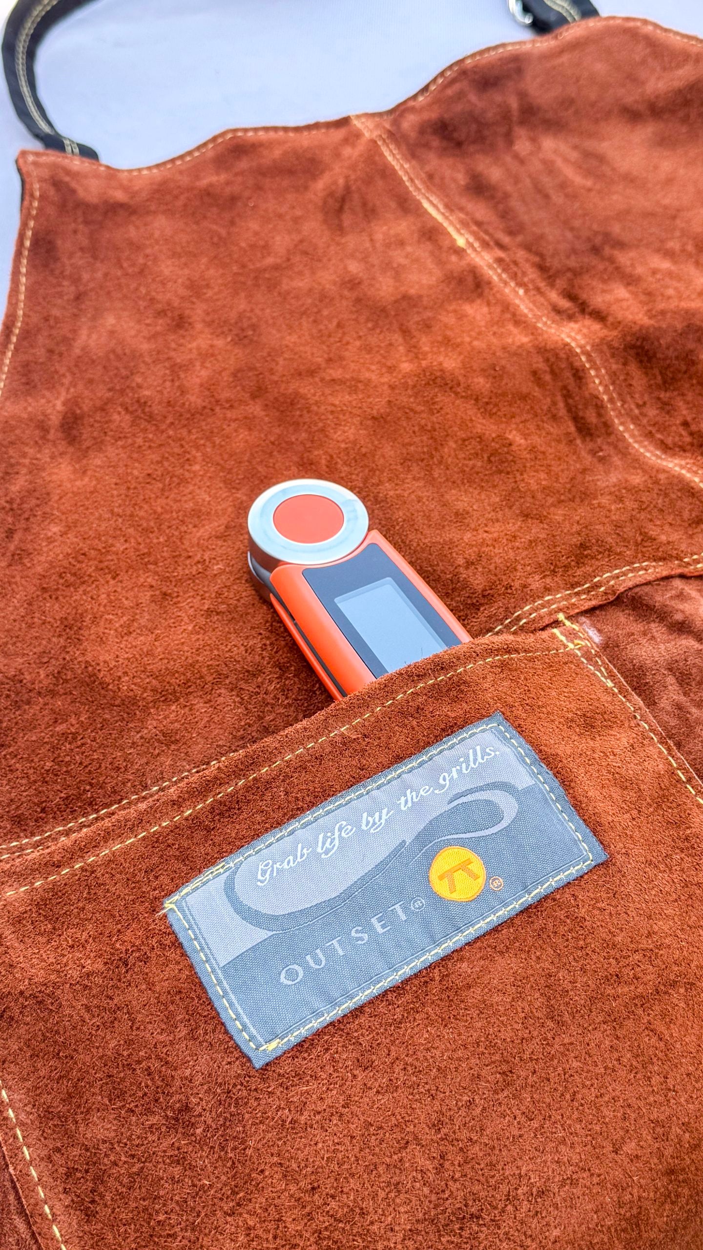 A close up of the brown leather Outset apron pocket that reads, "Grab Life by the Grills."