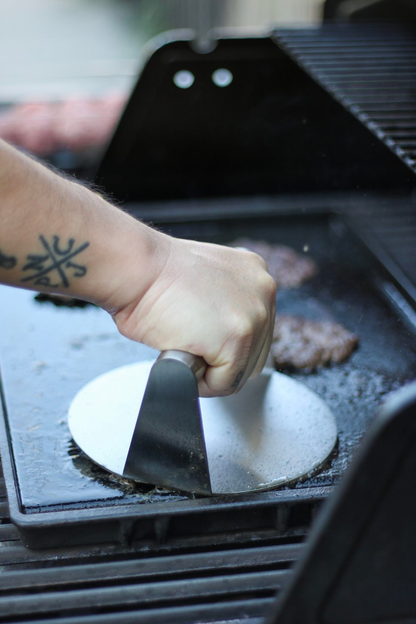 Darasak presses down on a ground beef burger ball to create a smash burger. He is using the Outset Premium grill press.