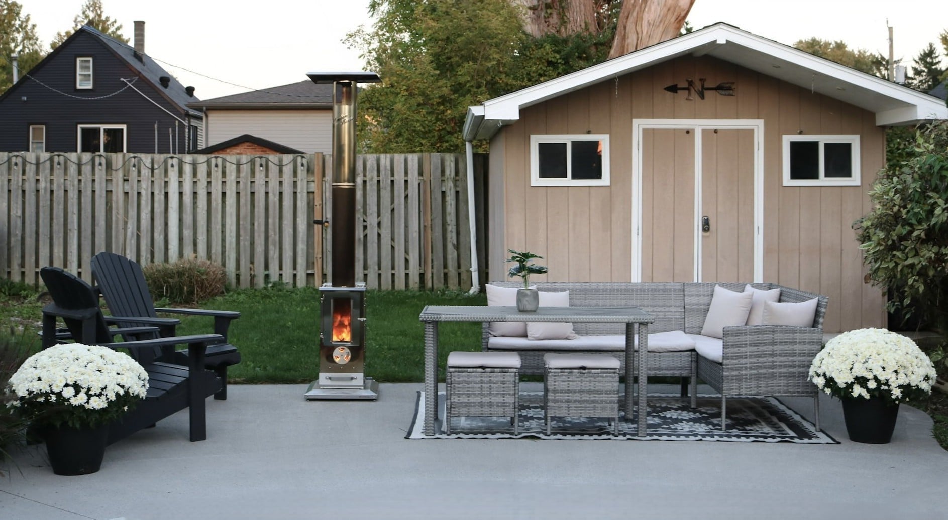 A Timber Stove 'Big Timber' sits on a patio with Adirondack chairs, a patio set and white mums. This article shares a Big Timber Review and why adding a Big Timber Patio Heater enhanced our backyard all season.