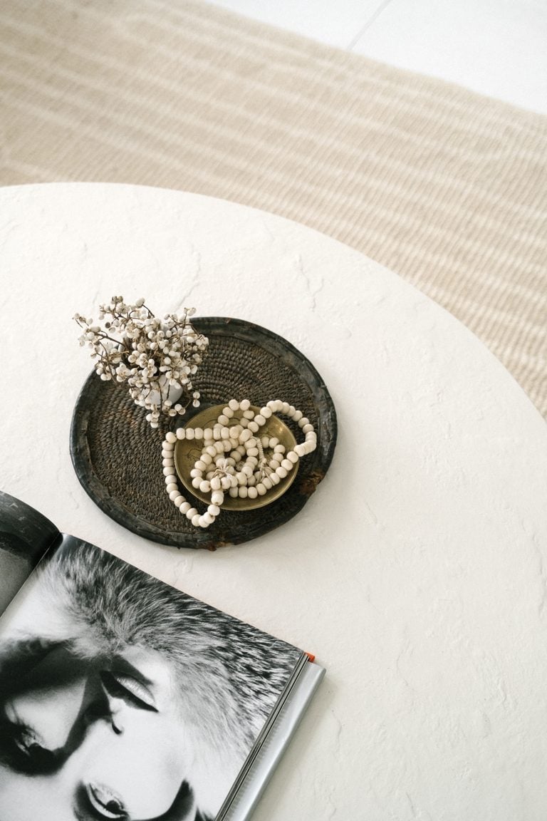 A minimalist still life depicting a necklace, dried flowers, and a book on a table, captured in soft lighting. This article shares a buyer's care guide for natural stone coffee tables.