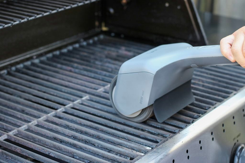 The Typhur Dome Electric Grill Brush Bot made the ultimate fall outdoor cooking and patio guide because it changes the clean-up game. A grill is shown with the bot being operated on the grill, cleaning the grate.